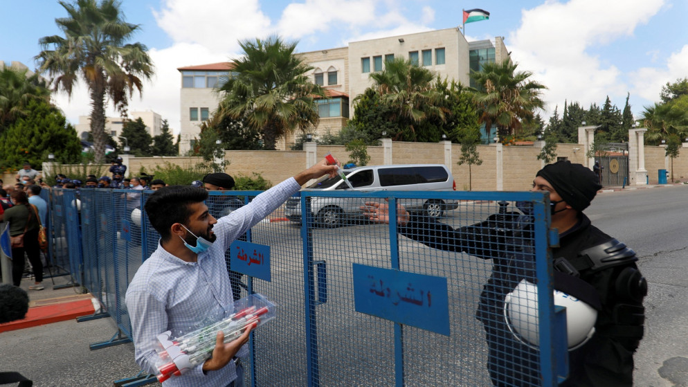 متظاهر فلسطيني يوزع أزهارًا اصطناعية على ضابط شرطة خلال تظاهرة تطالب بإعادة فتح المحلات التجارية المغلقة كجزء من قيود مرض فيروس كورونا (COVID-19)  .الضفة الغربية المحتلة .9 آب ، 2020.(رويترز / محمد توركمان)