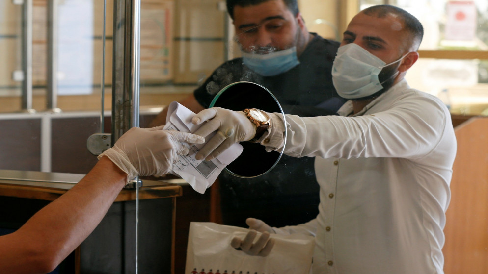مراجعان يرتديان كمامات وقفازات للوقاية من فيروس كورونا خلال إتمام معاملاتهما في مؤسسة رسمية في عمّان. أرشيفية. (محمد حامد/ رويترز)