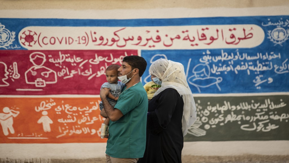 سوريان قرب جدارية توعوية بشأن الوقاية من فيروس كورونا المستجد في القامشلي في سوريا، 16 آب/أغسطس 2020. (دليل سليمان/ أ ف ب)