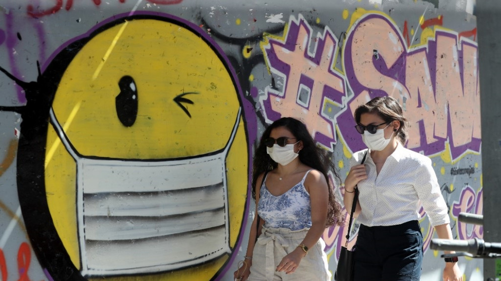 نساء يرتدين كمامات للوقاية من فيروس كورونا المستجد يمشين أمام لوحة غرافيتي تصور وجهًا مبتسمًا مع كمامات وجه في أنقرة التركية. 07/09/2020. (أ ف ب)