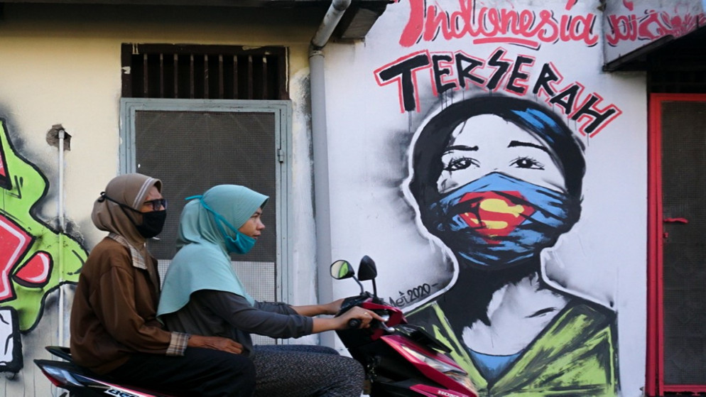 فتاتان على متن دراجة بخارية قرب لوحة جدارية في تانجيرانج في إندونيسيا، 23 أيار/مايو 2020. (أ ف ب)