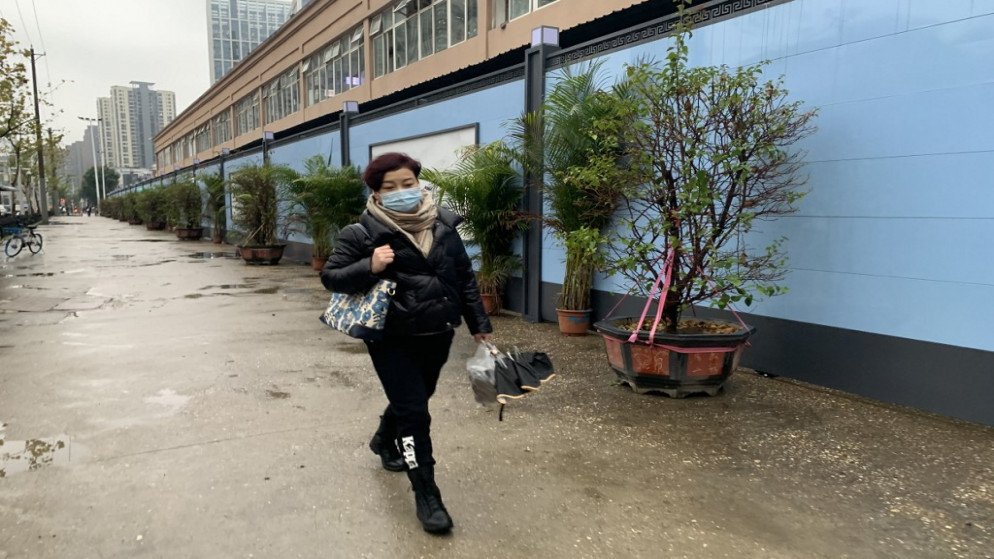 امرأة ترتدي كمامة كإجراء وقائي ضد فيروس كورونا وتسير بجوار سوق للمأكولات البحرية في ووهان في الصين. (أ ف ب)