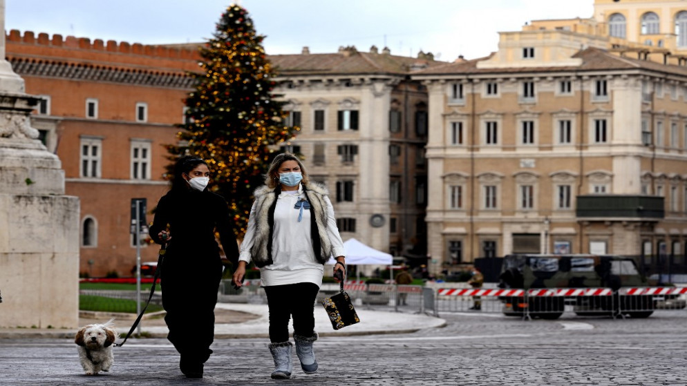 نساء يرتدين الكمامات ويسرن في ساحة بيازا فينيزيا الخالية في روما، 24 كانون الأول/ ديسمبر 2020 (أ ف ب)