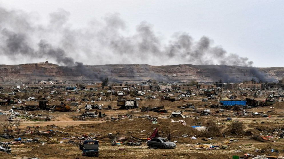 صورة أرشيفية لدخان يتصاعد خلف مركبات ومبان مدمرة في إحدى قرى محافظة دير الزور الشرقية السورية (أ ف ب)