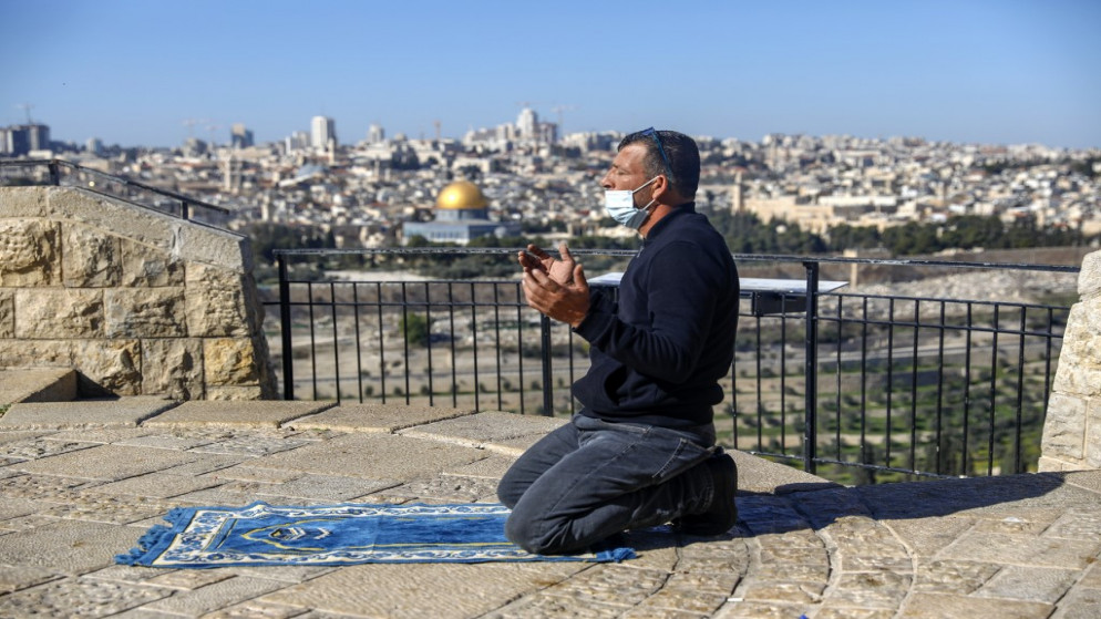 فلسطيني يرتدي كمامة طبية ويصلي على جبل الزيتون المطل على البلدة القديمة في القدس قرب المسجد الأقصى، 8 كانون الثاني/يناير 2021. (أحمد غرابلي/ أ ف ب)