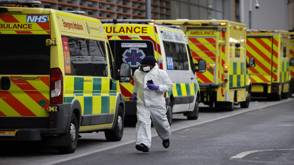 سائق يرتدي معدات الوقاية الشخصية بجانب خط من سيارات الإسعاف المتوقفة خارج مستشفى لندن الملكي في لندن، 19 كانون الثاني/ يناير 2021 (أ ف ب)
