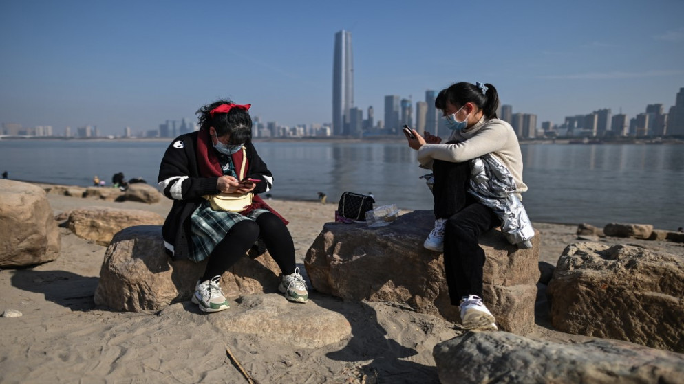 نساء يرتدين كمامات وجه للوقاية من فيروس كورونا المستجد ينظرن إلى هواتفهن المحمولة على ضفاف نهر اليانغتسي في ووهان الصينية. 19/01/2021. (هيكتور ريتامال / أ ف ب)