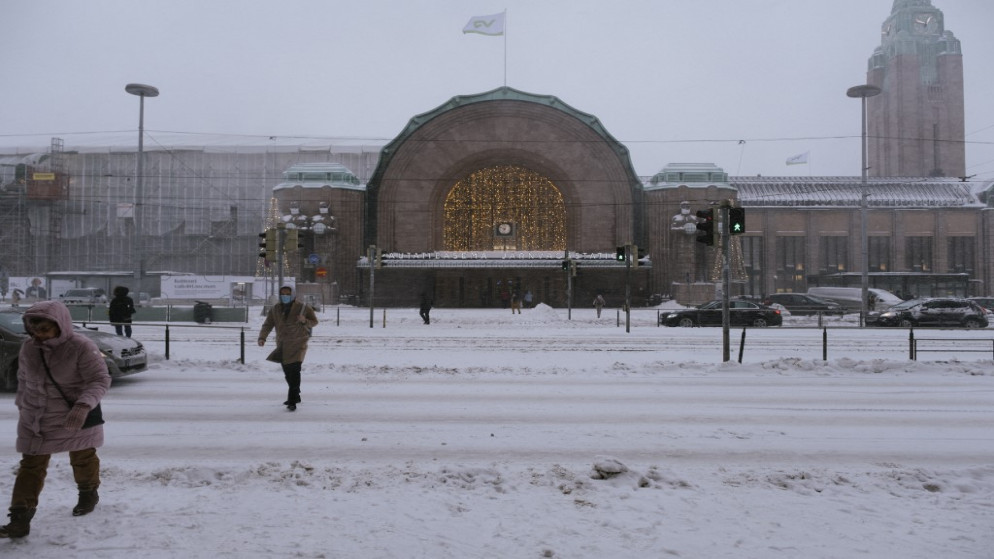 أشخاص يعبرون شارعا مغطى بالثلوج أمام المحطة المركزية في هلسنكي الفنلندية. 12/01/2021. (أ ف ب)