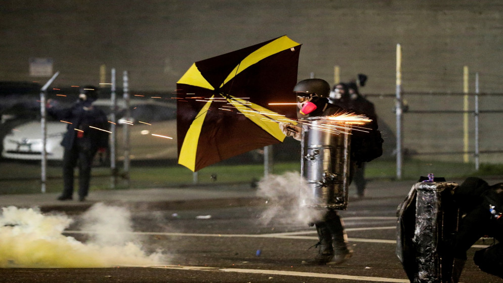 يستخدم أحد المتظاهرين مظلة ودرعًا بينما يستخدم ضباط إنفاذ القانون الفيدراليون ذخائر السيطرة على الحشود لتفريق المتظاهرين  بعد تنصيب الرئيس الأميركي جو بايدن.الولايات المتحدة. 20 يناير 2021. (رويترز)