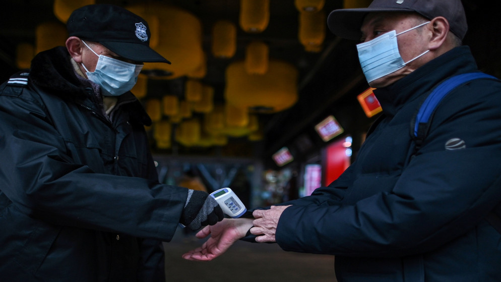 حارس يرتدي قناعًا للوجه كإجراء وقائي ضد فيروس كورونا يفحص درجة حرارة شخص عند مدخل مركز تسوق صغير في ووهان. 22 يناير 2021. (أ ف ب)