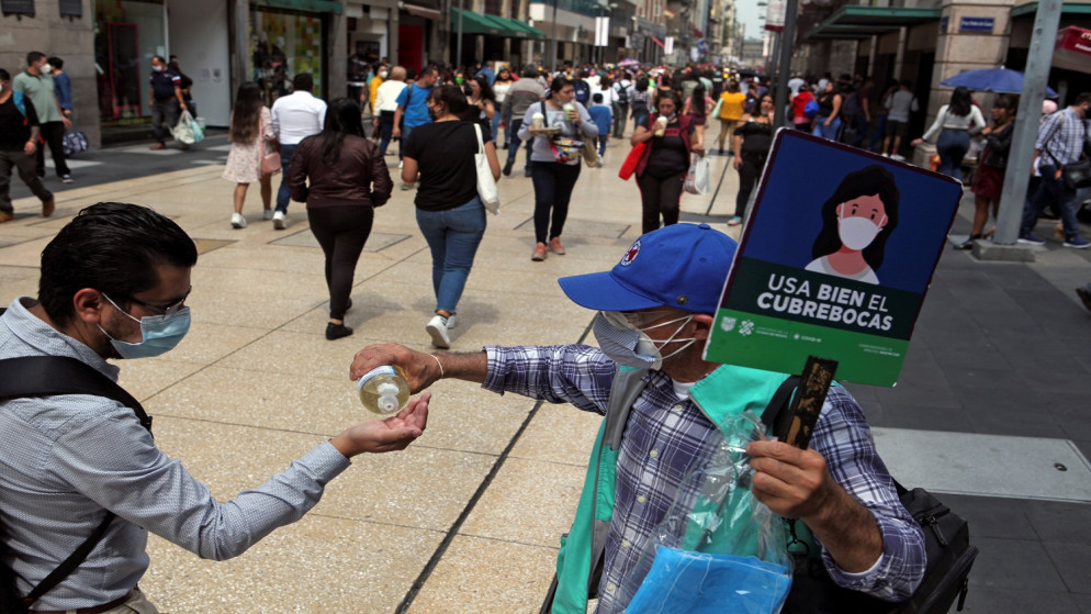 موظف حكومي يتقاسم المطهر مع أحد المشاة بينما يرفع لافتة تروج للاستخدام الصحيح للكمامات مع استمرار تفشي فيروس كورونا في المكسيك. 07/08/2021. (رويترز)