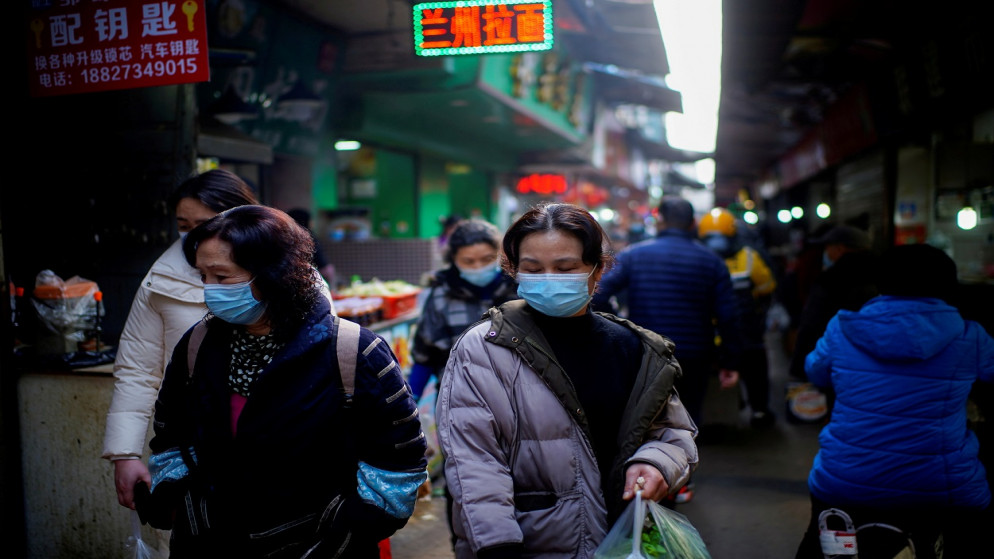 أشخاص يرتدون كمامات الوجه يسيرون في أحد أسواق الشوارع في الأشهر الأولى من تفشي الفيروس، في ووهان بمقاطعة هوبي بالصين، 8 شباط/ فبراير 2021. (رويترز)