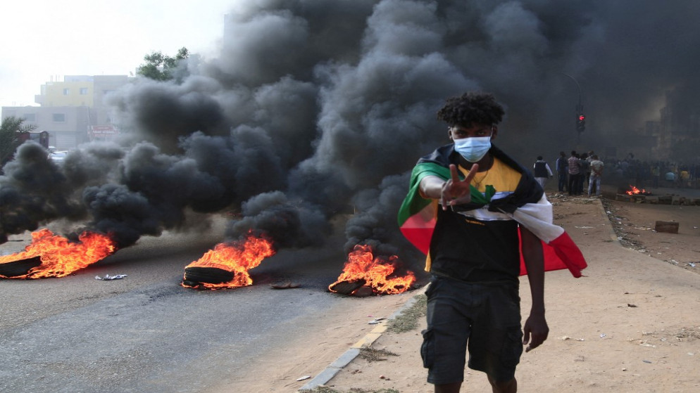 متظاهر سوداني وحوله العلم الوطني ويرفع علامة النصر بجوار إطارات محترقة خلال مظاهرة بالعاصمة السودانية الخرطوم، 25 أكتوبر / تشرين الأول 2021 (رويترز)