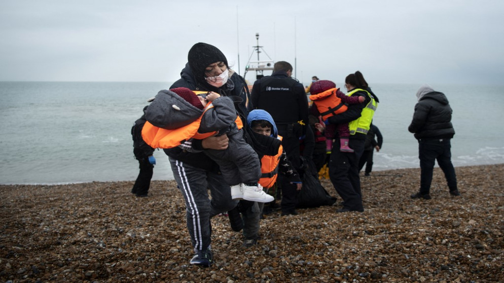 مهاجرة تحمل أطفالها بعد مساعدتها على الشاطئ من قارب نجاة RNLI (المؤسسة الملكية الوطنية لقوارب النجاة) على شاطئ في Dungeness ، على الساحل الجنوبي الشرقي لإنجلترا . 24 نوفمبر 2021. (أ ف ب)
