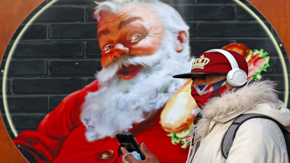 شخص يرتدي كمامة تحمل علم بريطانيا ويمشي بجوار صورة سانتا كلوز في سوق الكريسماس بوسط لندن، 29 تشرين الثاني/نوفمبر 2021. (أ ف ب)