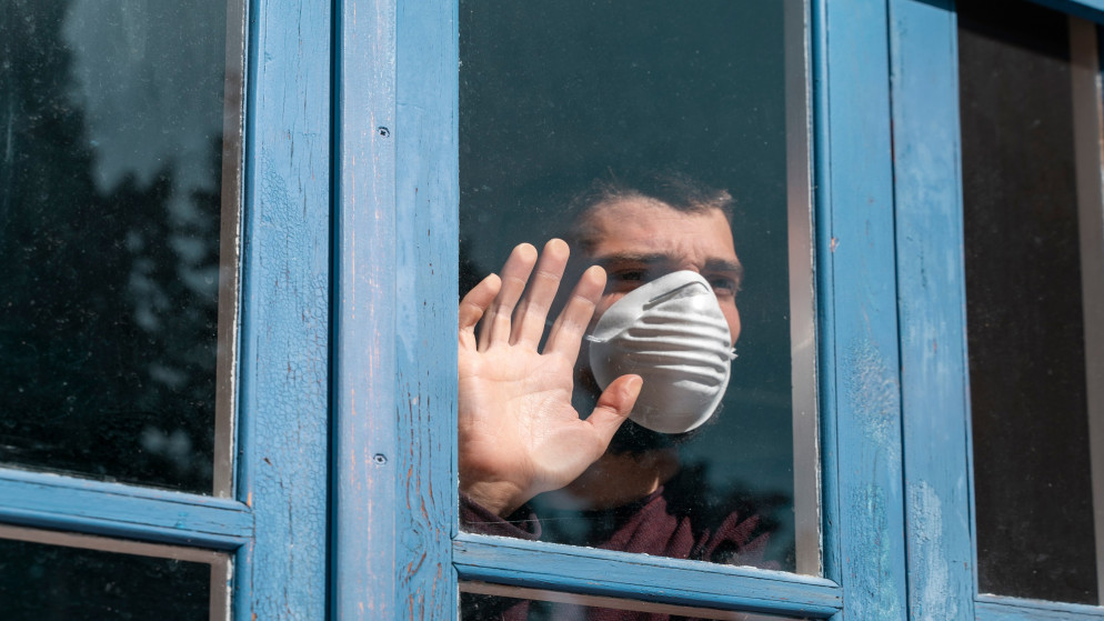 صورة توضيحية لرجل يرتدي كمامة للوقاية من كورونا ينظر من نافذة. (shutterstock)