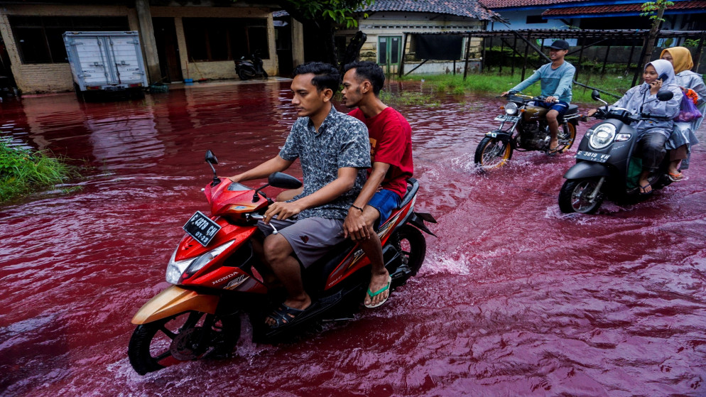 أشخاص يركبون دراجات نارية عبر طريق غمرته المياه الحمراء بسبب غمر الفيضانات لأصباغ الباتيك في بيكالونغان، مقاطعة جاوا الوسطى في إندونيسيا، 6 شباط/فبراير 2021. (رويترز)