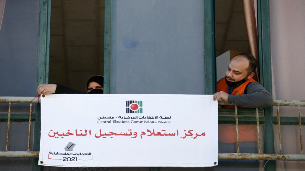 أعضاء لجنة الانتخابات المركزية الفلسطينية يعلقون لافتة مكتوب عليها "مركز استعلام وتسجيل الناخبين" في مدينة الخليل بالضفة الغربية المحتلة. 10/02/2021. (أ ف ب)