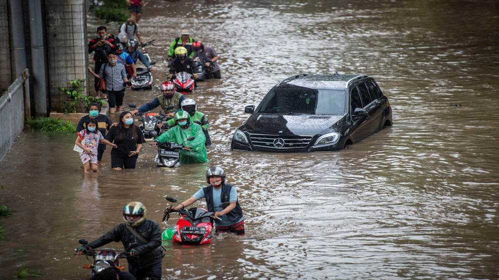 أشخاص يدفعون دراجاتهم النارية عبر المياه في منطقة تضررت من الفيضانات بعد هطول أمطار غزيرة في جاكرتا ، إندونيسيا ، 20 فبراير 2021.(رويترز)