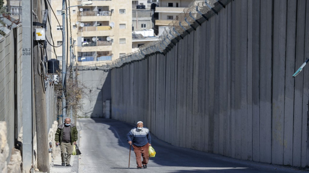 رجال فلسطينيون يسيرون بجوار الحاجز الإسرائيلي المثير للجدل الذي يفصل بين مدينة أبو ديس بالضفة الغربية (في الخلفية) والقدس الشرقية (في المقدمة) ، 16 فبراير ، 2021. (أ ف ب)