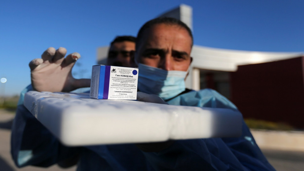 عامل صحي فلسطيني يعرض صندوقًا من لقاح كورونا الروسي، الذي أرسلته الإمارات العربية المتحدة، وسط تفشي فيروس، عند معبر رفح في جنوب قطاع غزة، 21 شباط/ فبراير 2021. (رويترز)