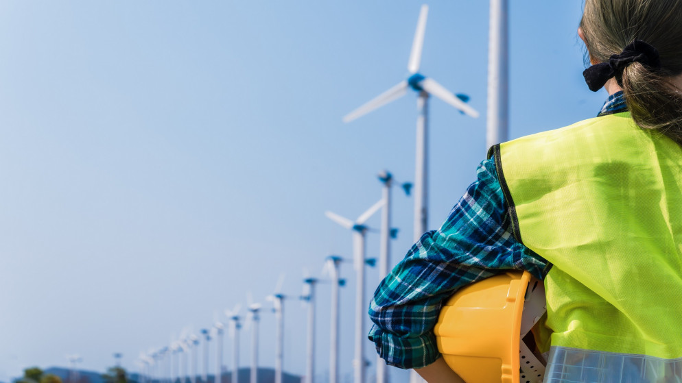 صورة توضيحية لمهندسة تعمل في مجال الطاقة المتجددة تقف بالقرب من توربينات الرياح المولدة للطاقة الكهربائية. (shutterstock)