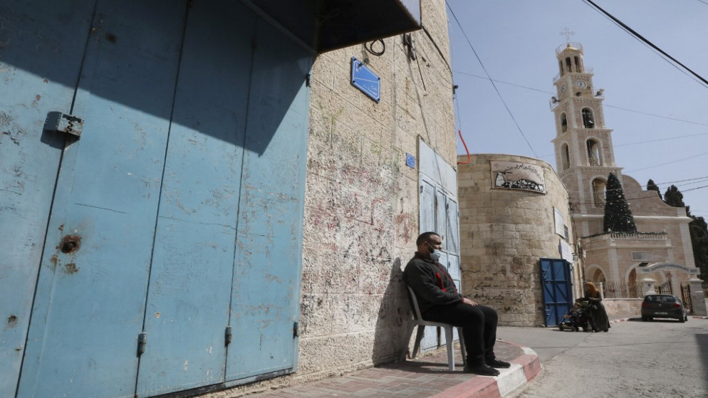 فلسطيني يرتدي كمامة واقية يجلس خارج متجر مغلق في بلدة بيت ساحور في الضفة الغربية المحتلة، 24 فبراير/شباط 2021. (حازم بدر/ أ ف ب)