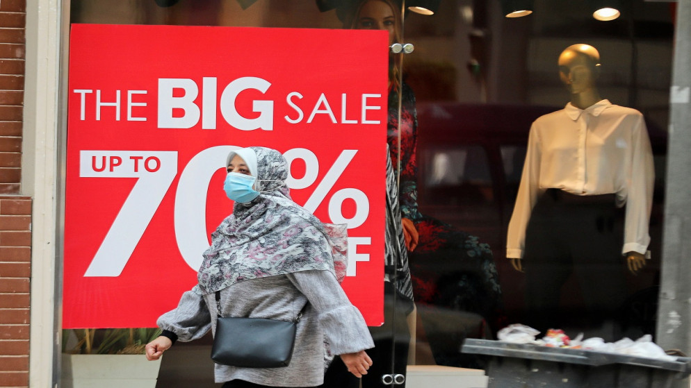 امرأة تمر عبر نافذة متجر لبيع الملابس تحمل لافتة تعلن عن تخفيضات على مبيعات الشتاء، وسط جائحة كورونا، القاهرة ، مصر ، 25 شباط/ فبراير 2021. (رويترز)