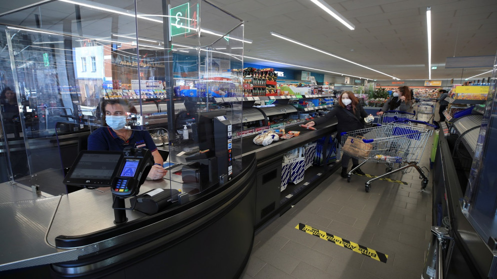 بائع في متجر طعام ألماني، خلف زجاج الحماية من COVID-19، وسط تفشي جائحة كورونا، إيسن بألمانيا، 5 آذار/ مارس 2021. (رويترز)
