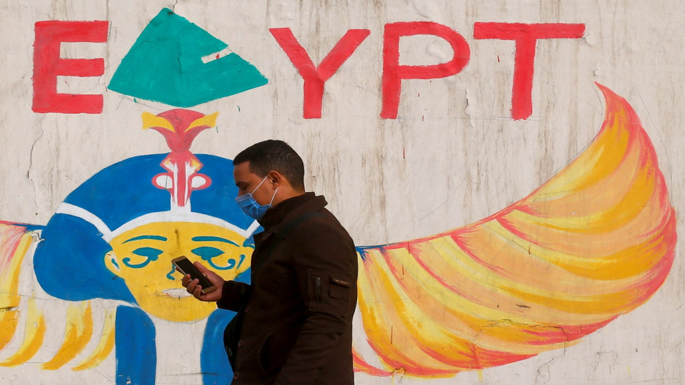 شخص يرتدي الكمامة ويسير أمام حائط مرسوم عليه صور فرعونية في القاهرة. مصر. 16/2/2021. (رويترز)