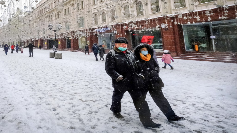 امرأة ورجل يرتديان قناع الوجه الواقي من جائحة "Covid-19" ، يمشيان تحت الثلج في أحد شوارع وسط موسكو في 21 شباط/فبراير 2021. (يوري كادوبنوف / أ ف ب)