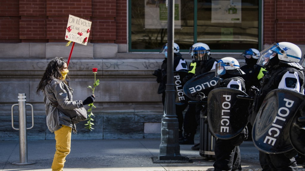 سيدة تشارك في احتجاج ضد إجراءات إغلاق كوفيد-19 في كيبيك إلى جانب الوجود المكثف للشرطة في مونتريال بكندا. 20/03/2021. (أندريه إيفانوف / أ ف ب)