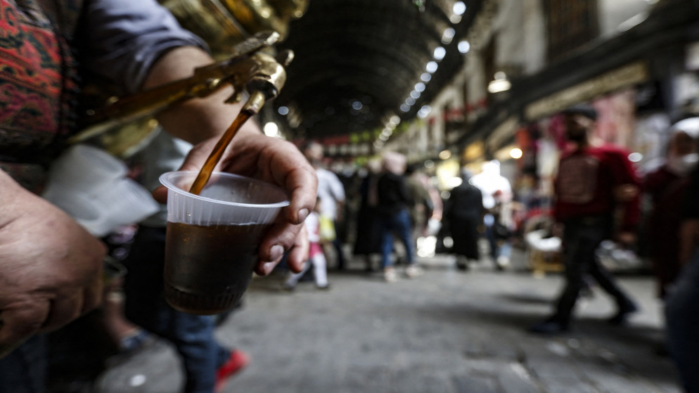 إسحاق كريميد، بائع عصير تمر هندي يصب بعض التمر الهندي لأحد الزبائن في سوق الحميدية بدمشق. 08/04/2021. (لؤي بشارة / أ ف ب)