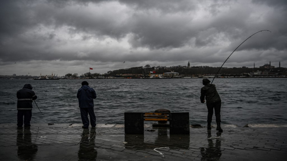 الناس يصطادون على شاطئ مضيق البوسفور في 8 أبريل 2020 خلال يوم ممطر بالقرب من ميناء كاراكوي في اسطنبول.(أ ف ب)