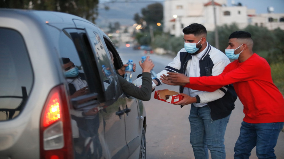 شبان مسيحيون من بلدة الزبابدة جنوب جنين يقدمون الماء والتمر للمارة أمام مدخل البلدة بعد دخول موعد الإفطار. 17/04/2021. (عدي دعيبس/ وفا)