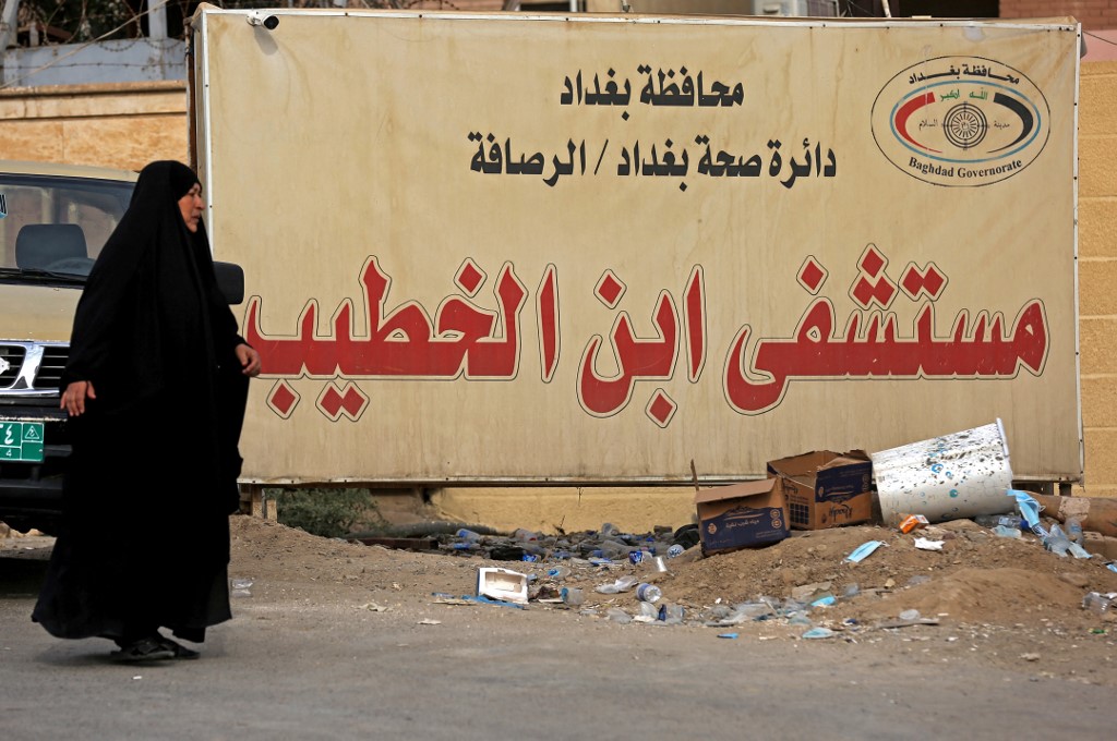 امرأة أمام لافتة لمستشفى ابن الخطيب في بغداد. (أ ف ب)