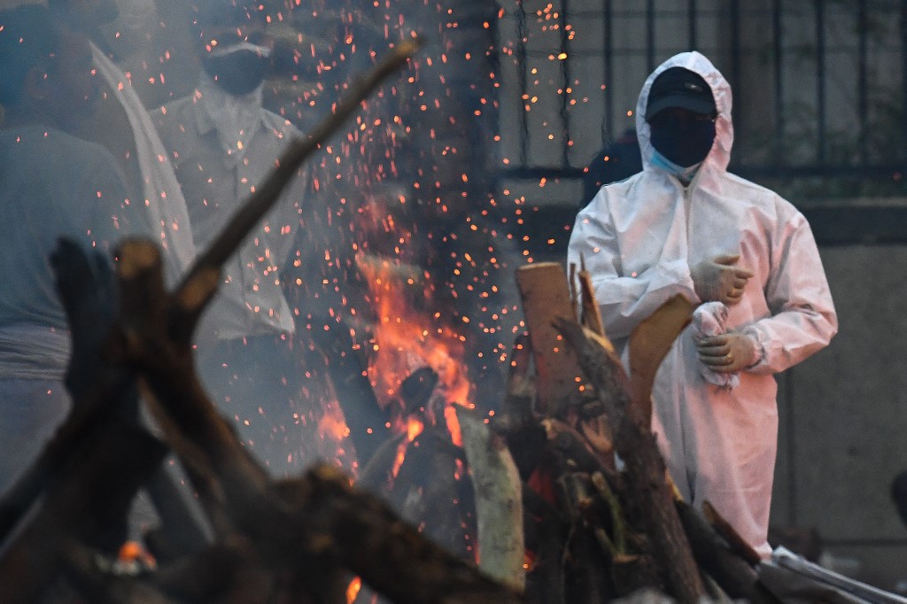 رجل يرتدي بدلة معدات الحماية الشخصية يقف بجانب محرقة جنازة قريبه الذي توفي بسبب فيروس كورونا  في موقع حرق الجثث في نيودلهي .6 مايو/أيار 2021 .(براكاش سينغ /أ ف ب)
