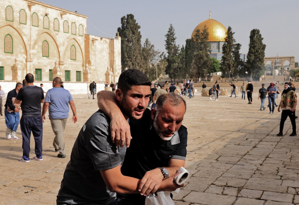 فلسطيني يساعد متظاهرا مصابا وسط مواجهات مع قوات الاحتلال الإسرائيلية في المسجد الأقصى بالقدس. 10/05/2021. (أحمد غربلي / أ ف ب)