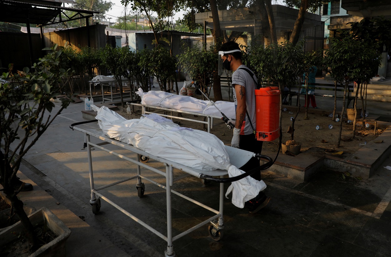 عامل يرش مطهرا على جثث الضحايا الذين لقوا حتفهم بسبب فيروس كورونا، نيودلهي، الهند، 10 مايو/أيار 2021. (رويترز)