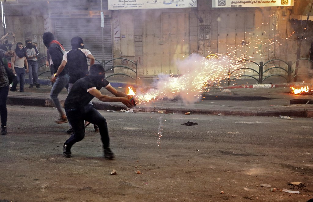 متظاهر فلسطيني يطلق قنابل إنارة وسط اشتباكات مع جنود الاحتلال الإسرائيلي وسط مدينة الخليل بالضفة الغربية المحتلة. 14 مايو 2021.(أ ف ب)