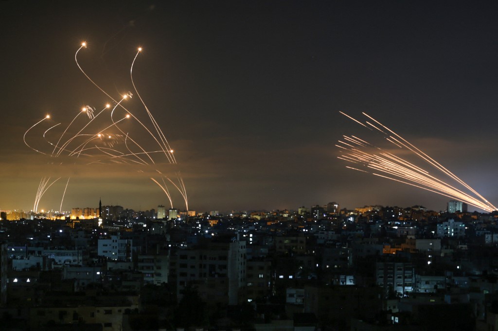نظام القبة الحديدية الإسرائيلي (يسار) يحاول اعتراض صواريخ المقاومة الفلسطينية (يمين) في سماء قطاع غزة، 14 أيار/مايو 2021. (أنس البابا/ أ ف ب)