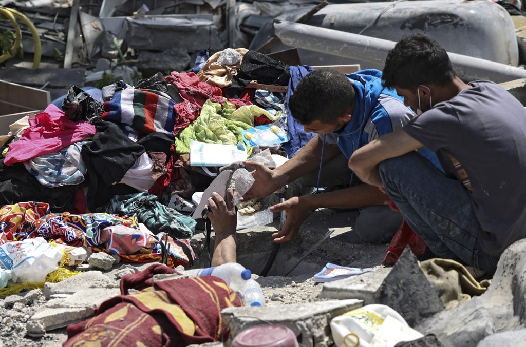 فلسطينيان يبحثان عن أحياء تحت أنقاض مبنى مدمر في حي الرمال السكني في مدينة غزة، 16 أيار/مايو 2021. (أ ف ب)