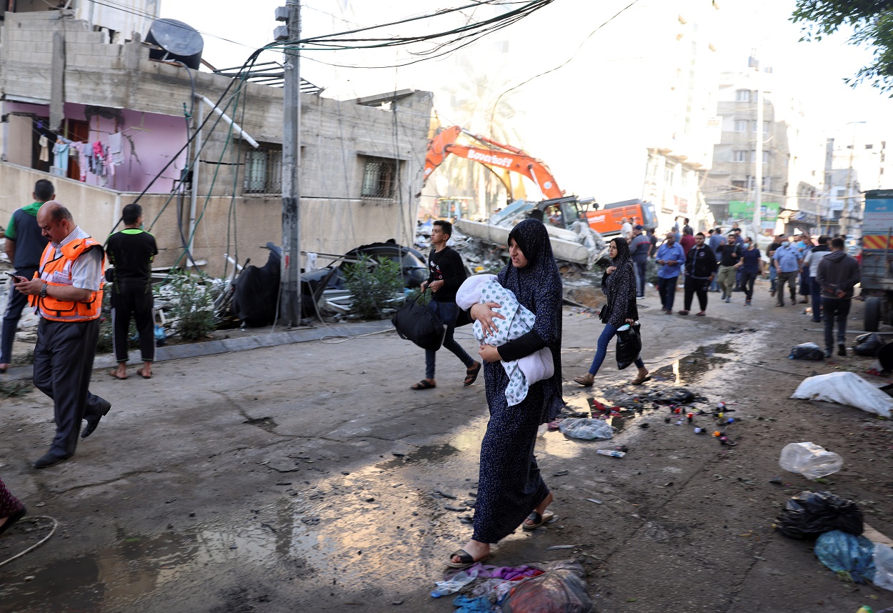 أشخاص يسيرون بالقرب من حطام في أحد شوارع مدينة غزة، 16 أيار/ مايو 2021. (رويترز)
