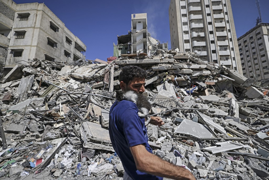 فلسطيني يحمل قطة مبنى مدمر في مدينة غزة، 18 أيار/مايو 2021. (محمود همص/ أ ف ب)