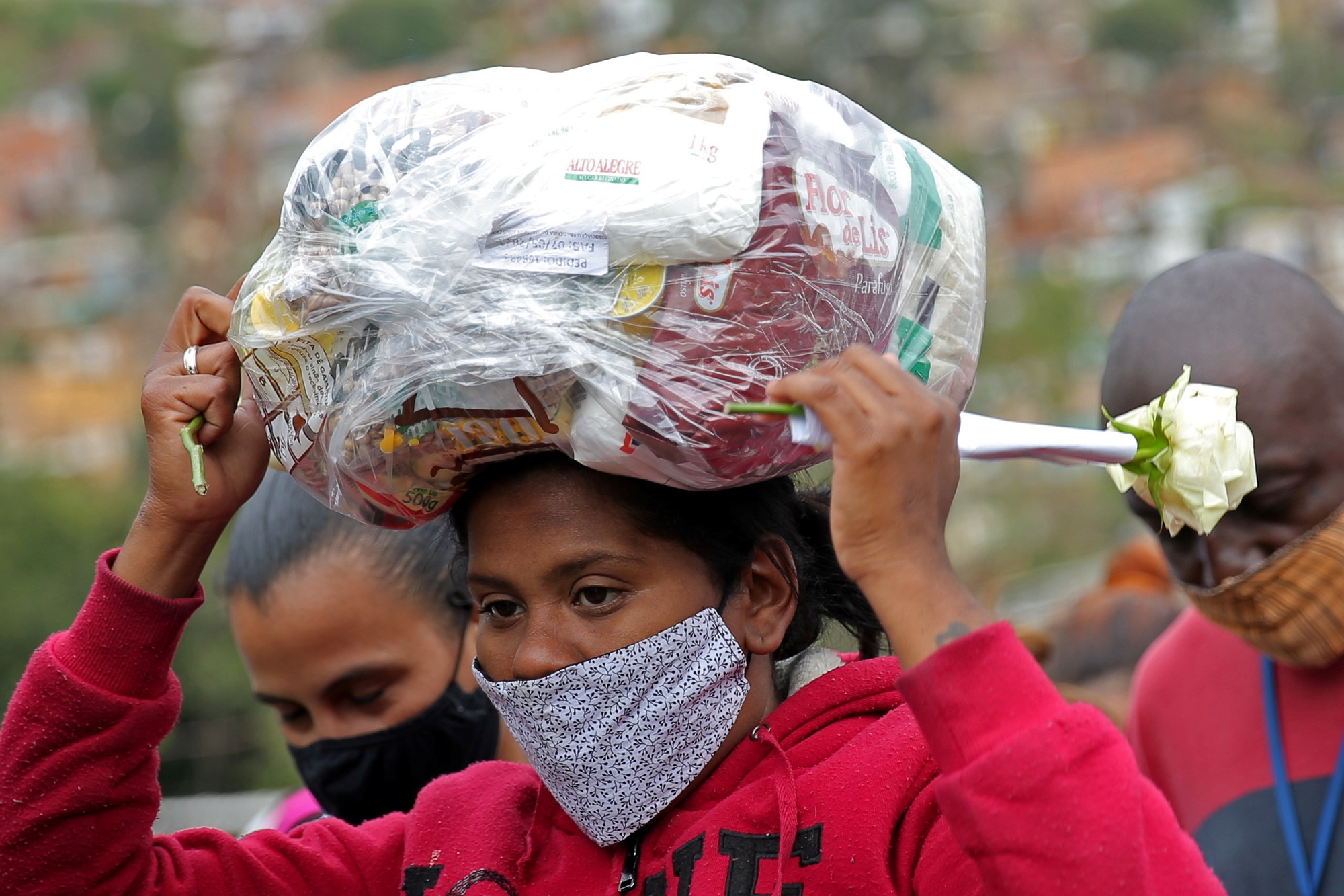 امرأة ترتدي كمامة وتحمل كيسا بلاستيكيا به معونة غذائية وزعته منظمة غير حكومية، وسط تفشي فيروس كورونا في البرازيل، 13 أيار/مايو 2021. (رويترز / كارلا كارنيل)