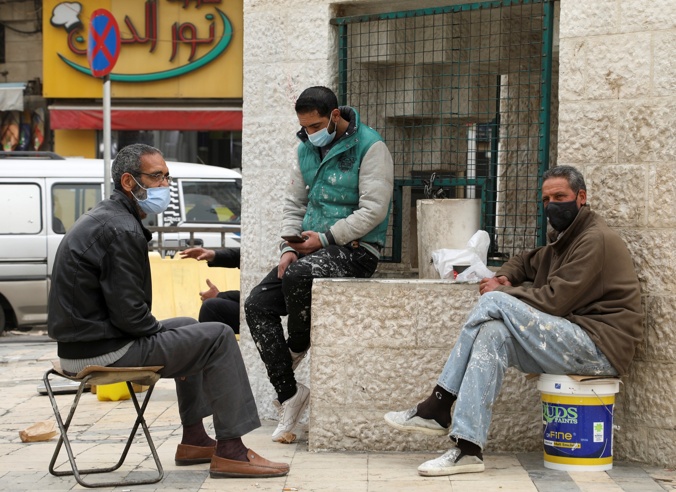 رجال يرتدون كمامات واقية ويجلسون في شارع في عمّان وسط مخاوف من انتشار فيروس كورونا، 23 مارس/آذار 2021. (علاء السخني/ رويترز)