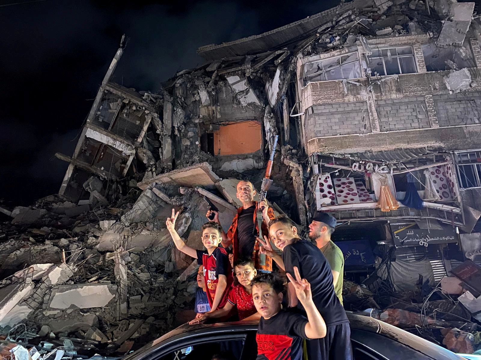 أشخاص يلوحون بالقرب من أنقاض مبنى مدمر بينما يحتفل الفلسطينيون في الشوارع بعد وقف إطلاق النار ، في مدينة غزة ، 21 مايو ، 2021. (رويترز / محمد سالم)