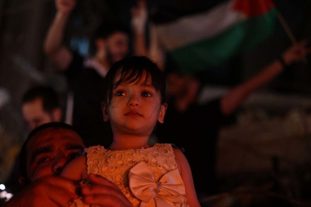 طفلة وأحد أفراد أسرتها ينضمون إلى الآخرين بينما يحتفل الناس في الشارع بعد وقف إطلاق النار في غزة، 20 أيار/مايو 2021. (أ ف ب)