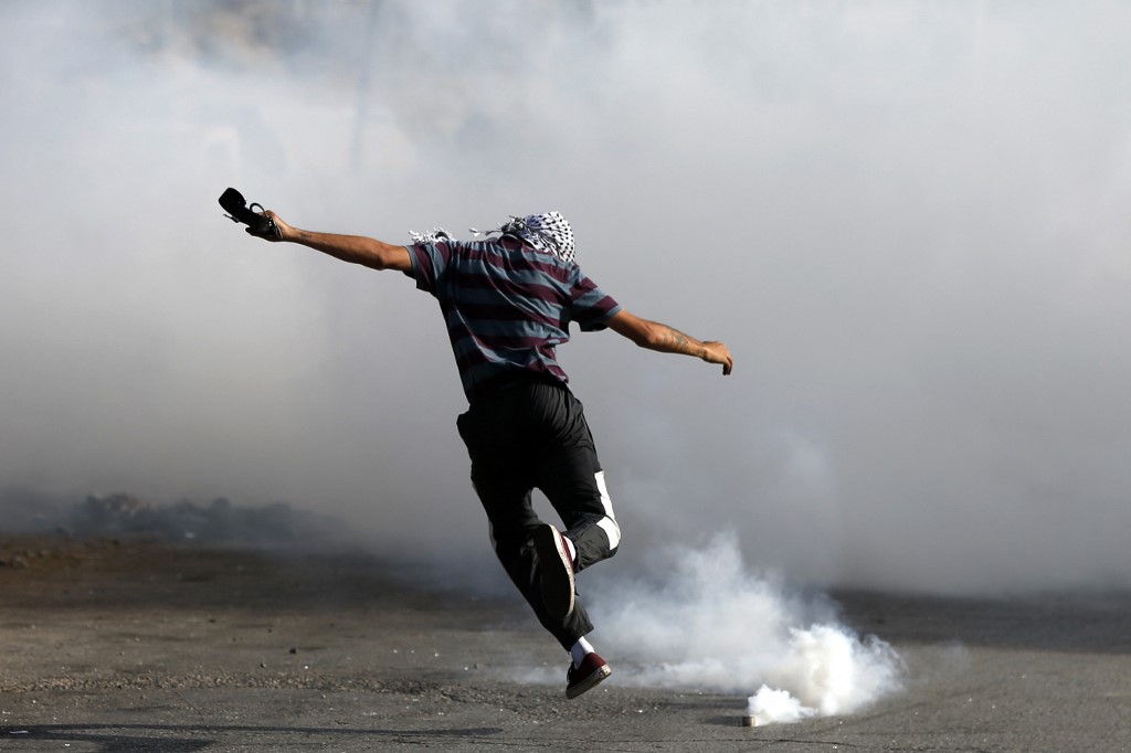 متظاهر فلسطيني يركل عبوة غاز مسيل للدموع وسط اشتباكات مع قوات الاحتلال الإسرائيلي بالقرب من مستوطنة بيت إيل بالقرب من رام الله في الضفة الغربية المحتلة .21 مايو/أيار 2021. (أ ف ب)