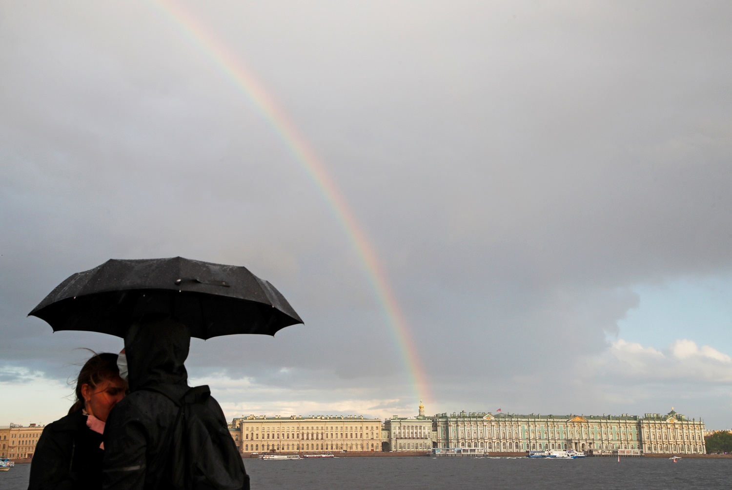 أشخاص يقفون على جسر بينما يظهر قوس قزح في السماء في سانت بطرسبرغ ، روسيا .22 أيار/مايو 2021. (رويترز)